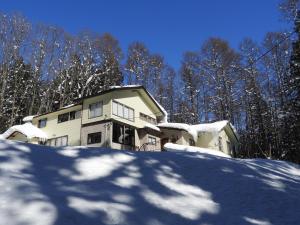 a house covered in snow in front of trees at Brocken Hutte in Hakuba