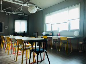 a room with tables and yellow chairs and windows at Sohostel Korea in Busan