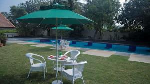 a table and chairs with a green umbrella next to a pool at Jungle Safari Resort & Holiday Villa in Nashik
