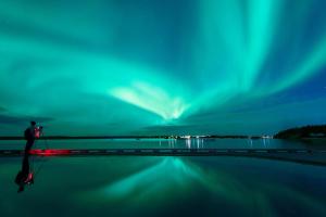 Um homem em cima de uma vedação a olhar para a aurora boreal. em Nova Inn Yellowknife em Yellowknife