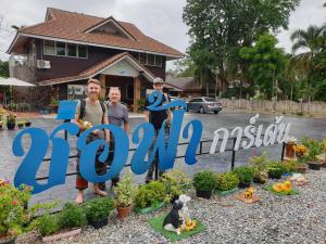 a group of people standing next to a sign that reads with plants at ช่อฟ้า การ์เด้น in Phrae