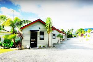 un pequeño edificio blanco con palmeras junto a una carretera en Tairua Shores Motel en Tairua
