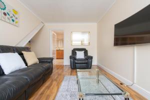 a living room with a black leather couch and a chair at Abkat Three Bedroom Home in London