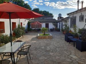un patio con mesas, sillas y una sombrilla roja en Apartamentos Rurales Fuente de Marzo, en Anna