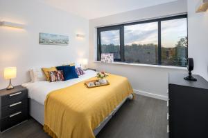 a bedroom with a bed with a yellow blanket and a window at St Albans City Apartments - Near Luton Airport and Harry Potter World in St. Albans