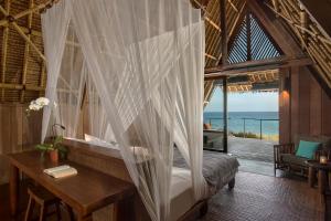 a bedroom with a bed and a desk with a view of the ocean at Jeeva Beloam Beach Camp in Tanjung Ringgit