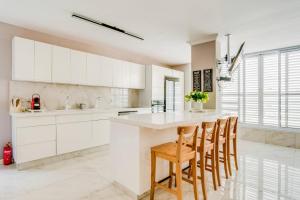 una cocina con armarios blancos y una isla con sillas en MAGNIFIQUE APPARTEMENT A 3' DE LA PLAGE ET KIKAR, en Netanya