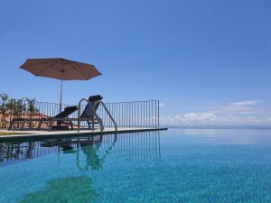 a swimming pool with an umbrella and chairs and the water at Casa Atlantico Dachterrassengeschoss in Ribeira Brava
