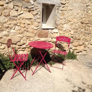 duas cadeiras vermelhas e uma mesa em frente a um edifício de pedra em Chambre d'hôte Geiko em Cabrières-dʼAigues