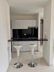 a kitchen with two white stools and a black counter at Sensacional Apartamento Reserva Peñon Girardot in Girardot