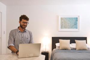 a man standing in front of a bed with a laptop at Ballantyne at Mosman - Serviced Apartments in Sydney