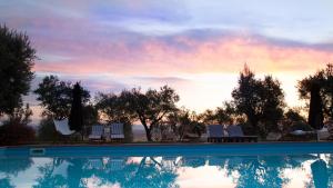 a pool with chairs and a sunset in the background at Villa Giuncheto in Corsano