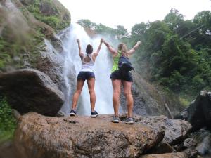 two women standing on a rock in front of a waterfall at Hotel Perico Azul & Surf Camp in Jacó