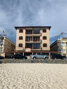 a building on the beach with cars parked in front of it at Pé na Areia in Arraial do Cabo