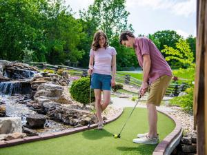 un homme et une femme jouant au golf dans un jardin dans l'établissement Luxury Lakefront Chalet Resort 2 Pools FREE Amenities Dock MiniGolf Waterslide, à Lampe