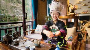 una mujer con una corona sosteniendo una taza en una habitación en Fenghuang Tujia Ethnic Minority River View Hotel, en Fenghuang