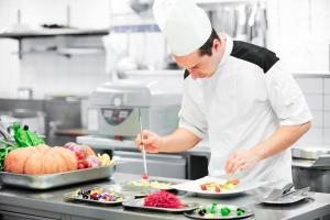 a chef preparing food in a kitchen with plates of food at Le Bristol Leukerbad in Leukerbad