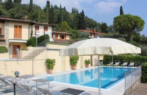 a pool with an umbrella and chairs and a house at Villa Belvedere in Gardone Riviera