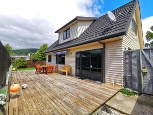 un patio trasero con una terraza de madera y una casa en Atarau Grove Holiday House, en Paraparaumu