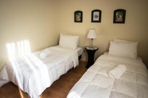 2 camas en una habitación con sábanas blancas en Departamentos Los Ganaderos, en Punta Arenas