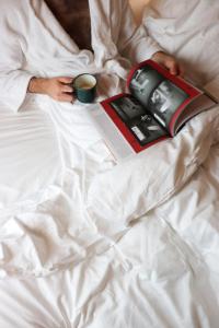 a man laying in bed with a book and a cup of coffee at Le Citizen Hotel in Paris