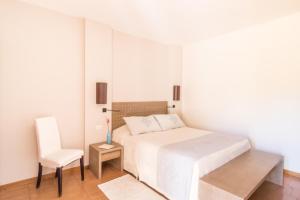 a white bedroom with a bed and a chair at Hotel Aquadulci in Chia
