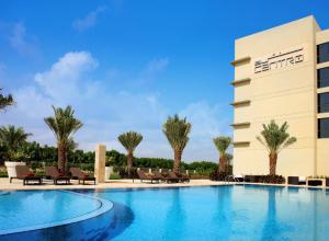 a hotel with a swimming pool and palm trees at Centro Sharjah in Sharjah