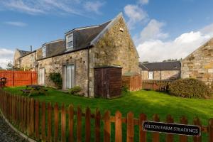 una antigua casa de piedra con una valla de madera en The Steadings - by StayDunfermline, en Dunfermline