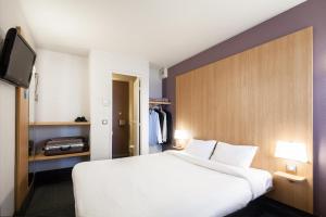 a bedroom with a large white bed and a tv at B&B HOTEL Maubeuge-Louvroil in Louvroil