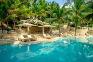 a swimming pool with chairs and umbrellas and palm trees at Swahili Beach in Diani Beach