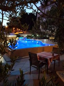 a table and chairs next to a swimming pool at night at Hotel Villa Džamonja in Bol