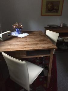 una mesa de madera con 2 sillas blancas y un jarrón de flores en Schönenborn, en Lindlar