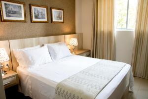 a bedroom with a large white bed and two lamps at APTO ACONCHEGANTE proximo ao centro in Foz do Iguaçu