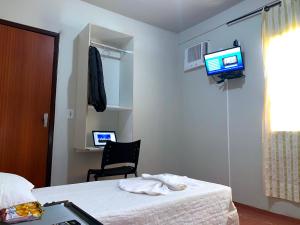 een slaapkamer met een bed, een stoel en een televisie bij Hotel Caçula in Londrina