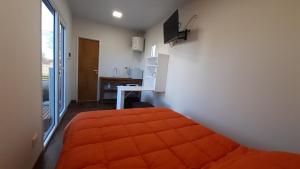 1 dormitorio con cama de color naranja y escritorio en LEKU Lodge & Deptos en General Acha