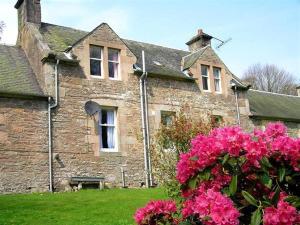 une maison en pierre avec des fleurs roses devant elle dans l'établissement Laundry Cottage, à Lanark