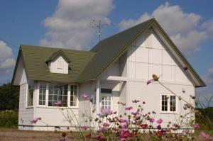 ein weißes Haus mit einem grünen Dach und Blumen in der Unterkunft Farm Inn Tsurui in Tsurui