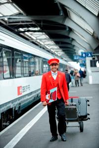 a man in a red jacket with a cart at a train station at Hotel Schweizerhof Zürich in Zurich