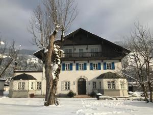 a large white house with a tree in the snow at Ferienwohnung Eiskögerl im Barbarahof in Bischofshofen