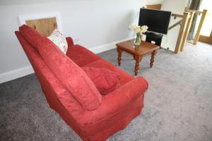 a red couch in a living room with a table at Superb Stokesby Barn Apartment - Norfolk Broads & Norwich in Stokesby