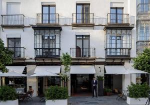 Un uomo in giacca e cravatta che si trova di fronte a un palazzo di EME Catedral Hotel a Siviglia