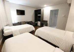 a hotel room with three beds and a television at Fratele Business Hotel in Patos de Minas