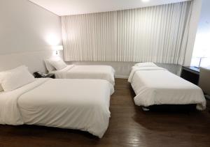 three beds in a hotel room with white sheets at Fratele Business Hotel in Patos de Minas