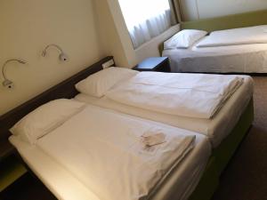 2 bedden in een hotelkamer met witte lakens bij Behringers City Hotel Nürnberg in Neurenberg