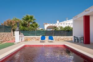 a swimming pool with two blue chairs and a house at Villa en Menorca in Mahón