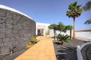 a stone wall and a walkway with palm trees at Las Perseidas in Costa Teguise
