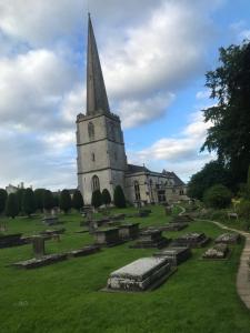 a church with a tall steeple on a green field at Dove Lodge in Painswick