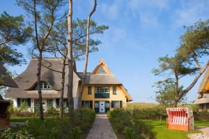 ein gelbes Haus mit einem Strohdach und einer Auffahrt in der Unterkunft Ferienwohnungen Dünenmeer in Dierhagen