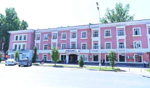 ein rosafarbenes Gebäude auf einer Straße mit einem Parkplatz in der Unterkunft Rohat Hotel in Duschanbe