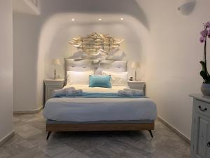 a white bedroom with a large bed with blue pillows at Iliovasilema Hotel & Suites in Imerovigli